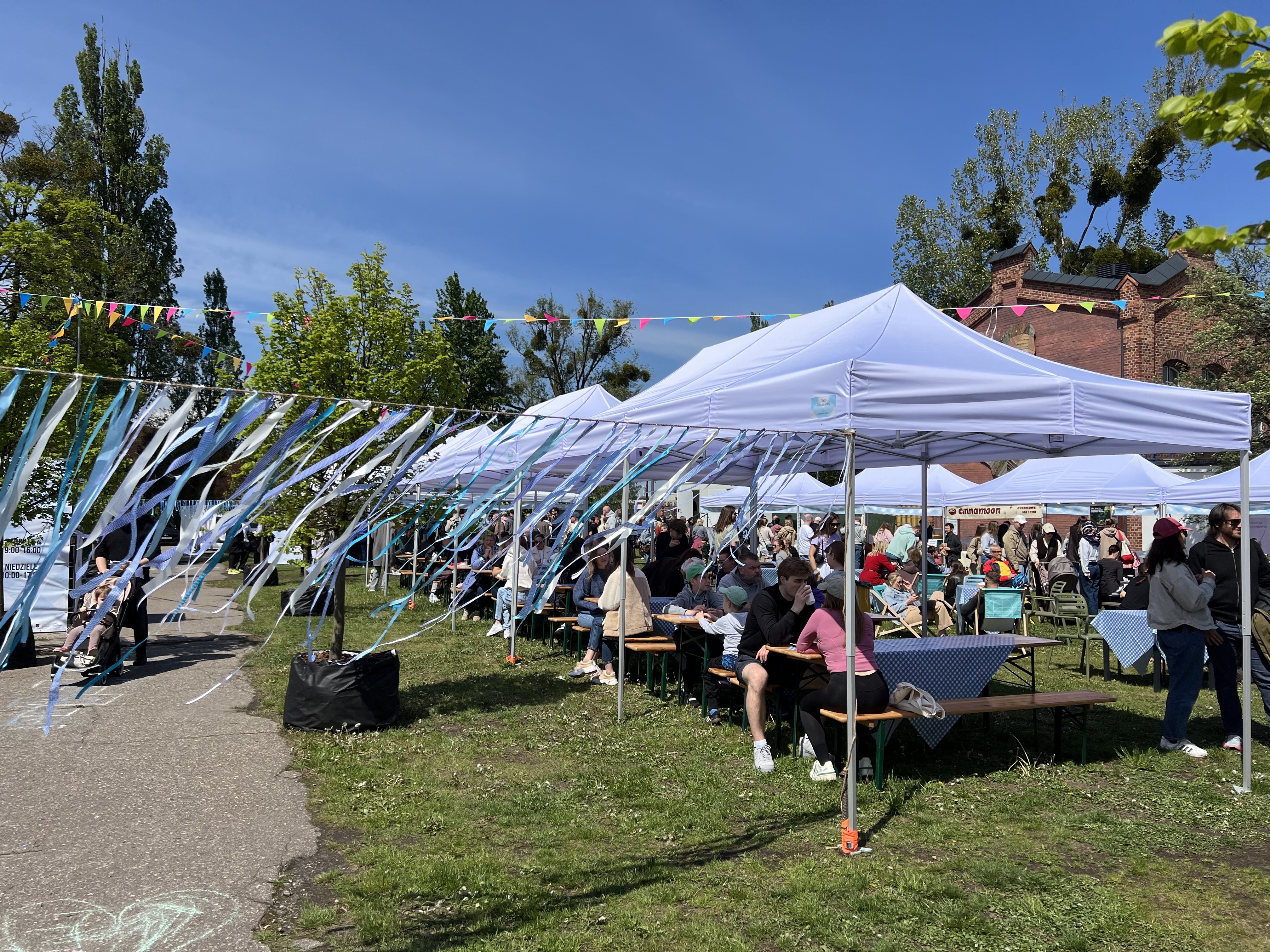 A spring market under white tents, blue-and-white ribbons, long checkered tables.