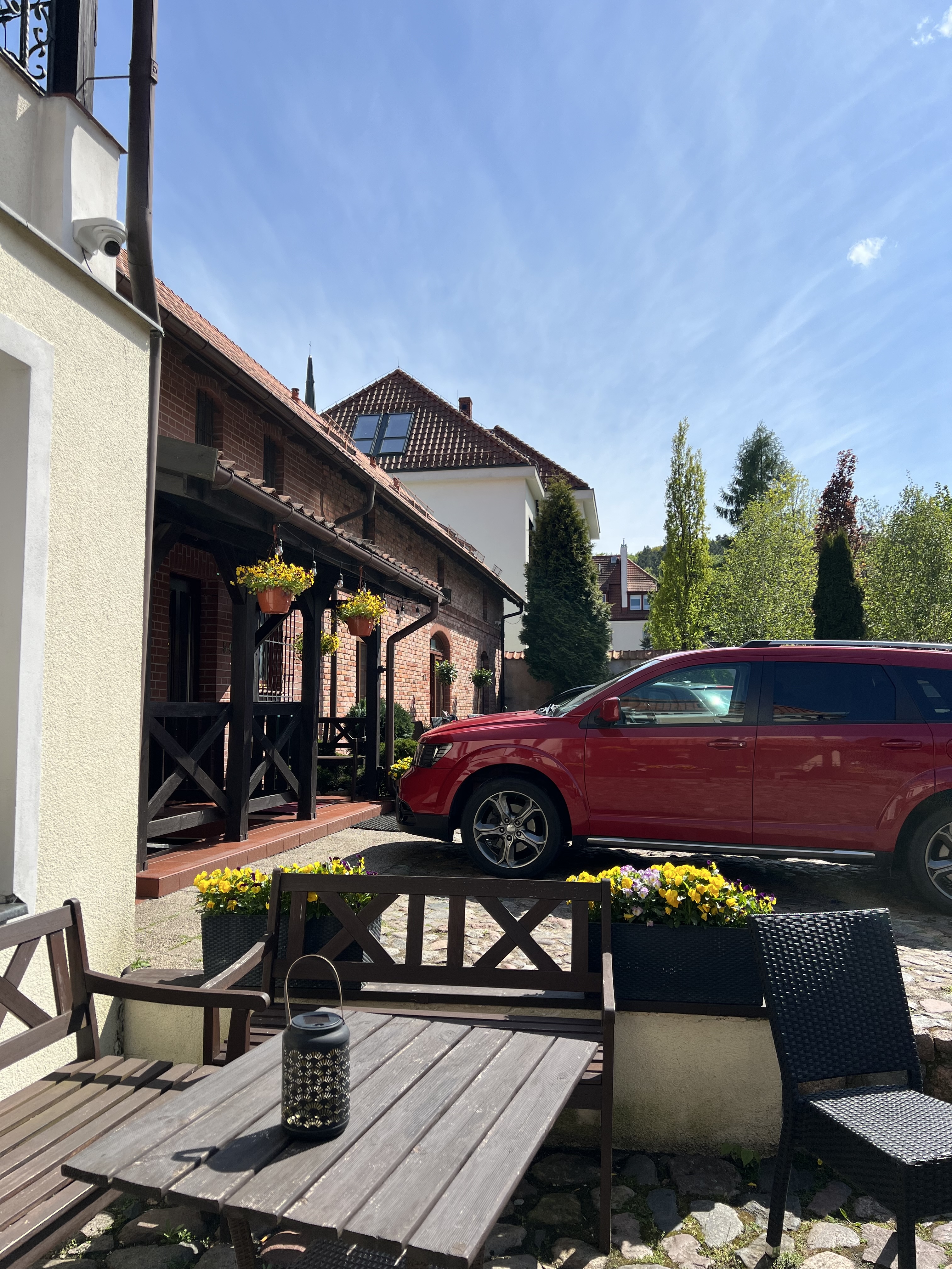 Oliwa Park Residence — brick, a wooden porch, baskets of yellow flowers, a red Dodge on the cobbles.