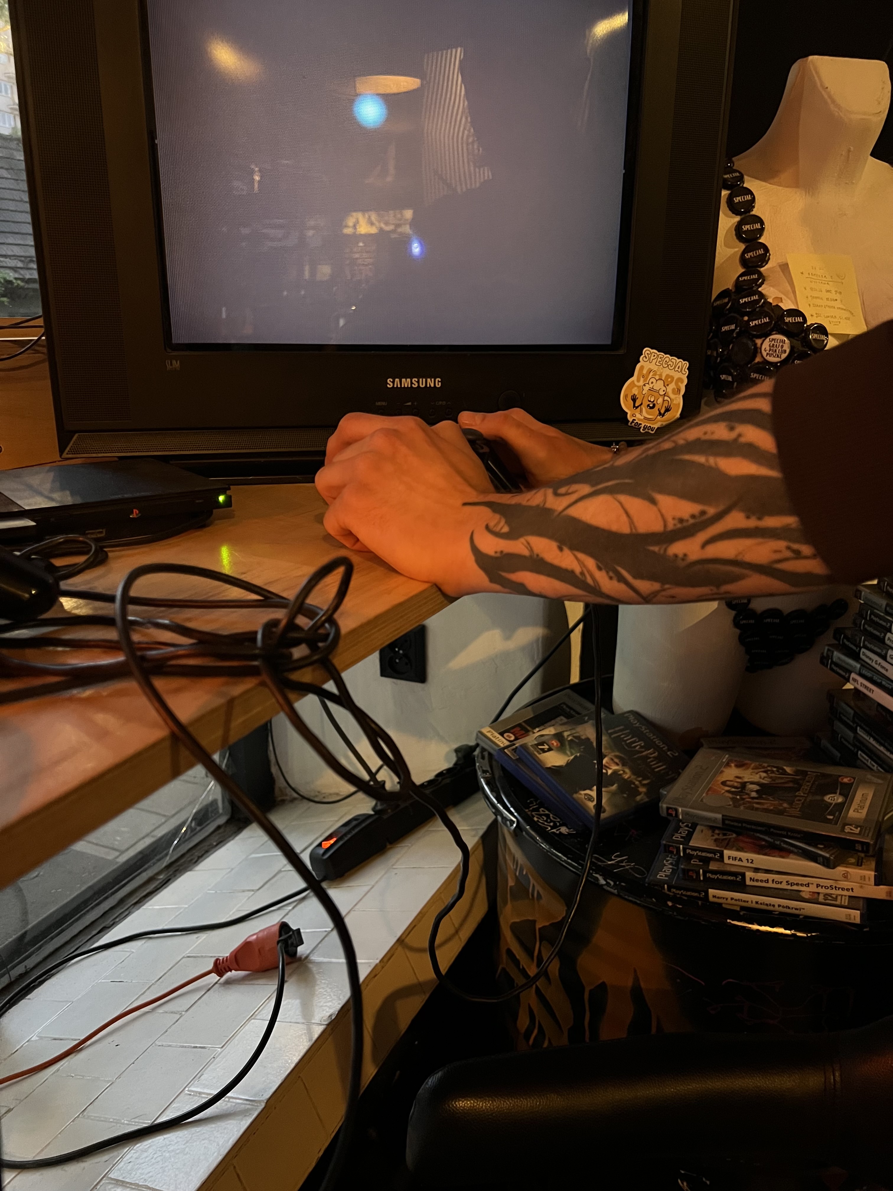A PlayStation 2 glowing into an old tube TV, a leaning tower of game cases beside it.