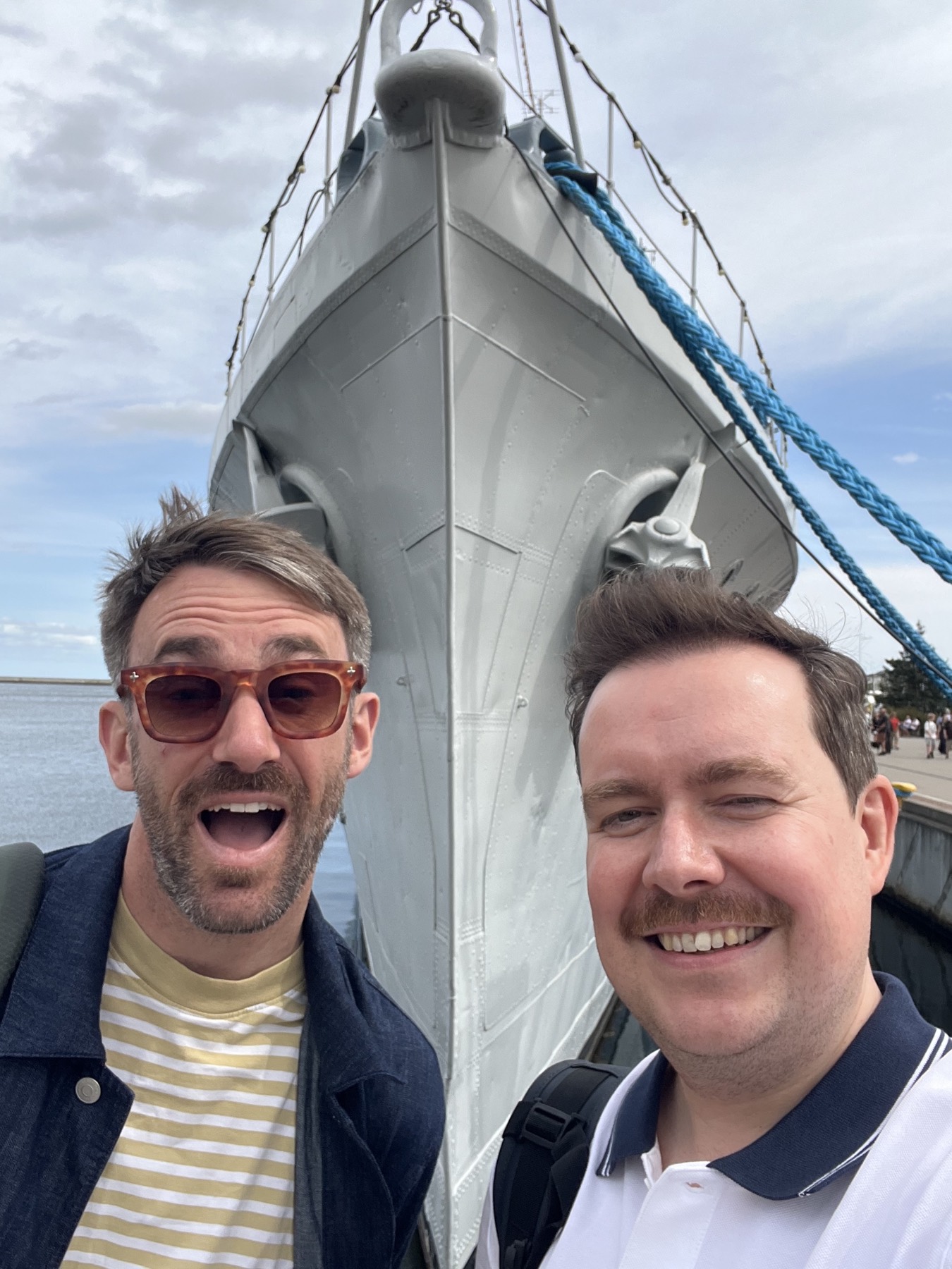 Lawrence and Alex in front of the bow of ORP Błyskawica, riveted steel rising overhead