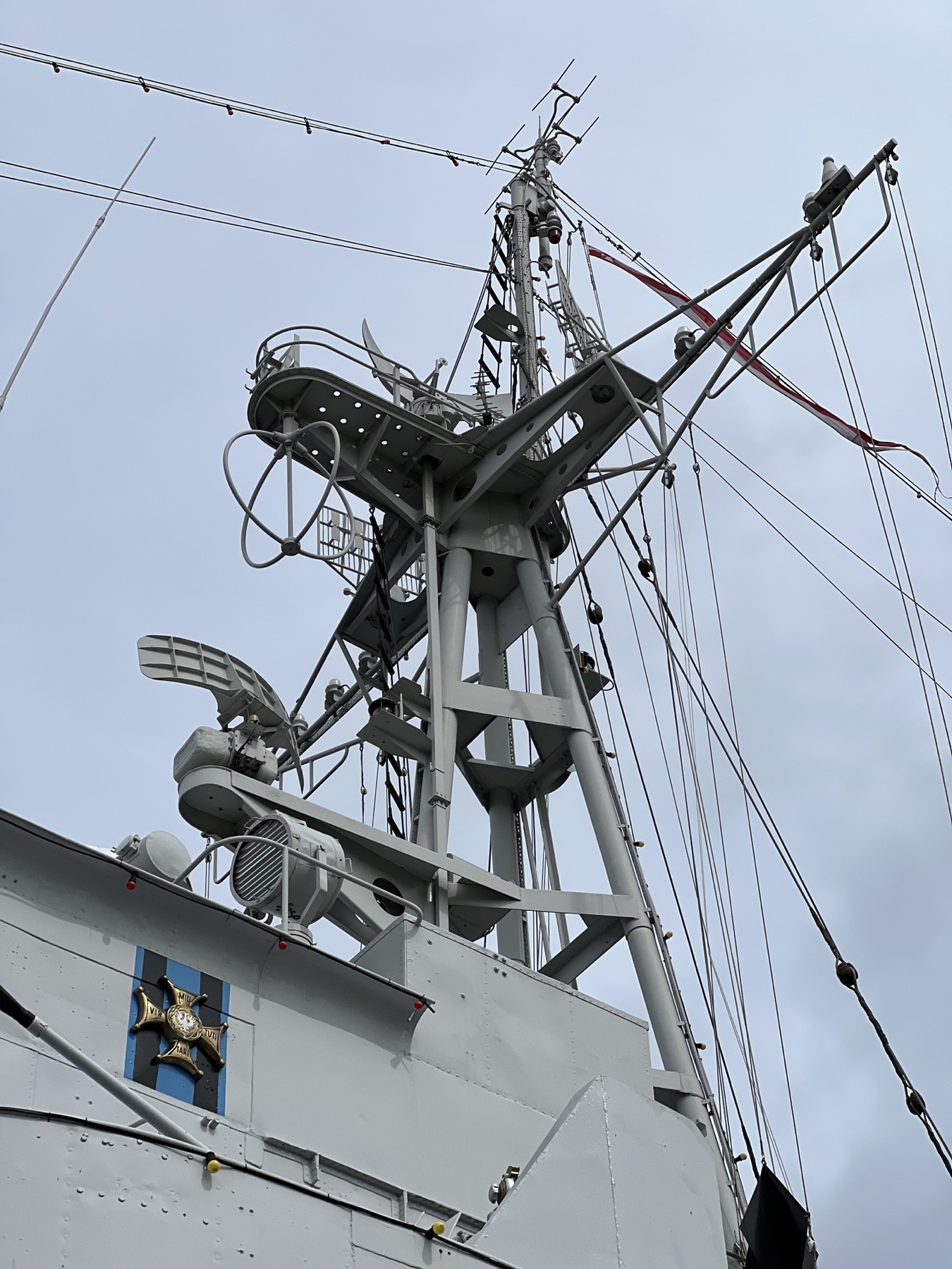 The mast of ORP Błyskawica — antenna rings, signal lines and a red-and-white flag against a gray sky